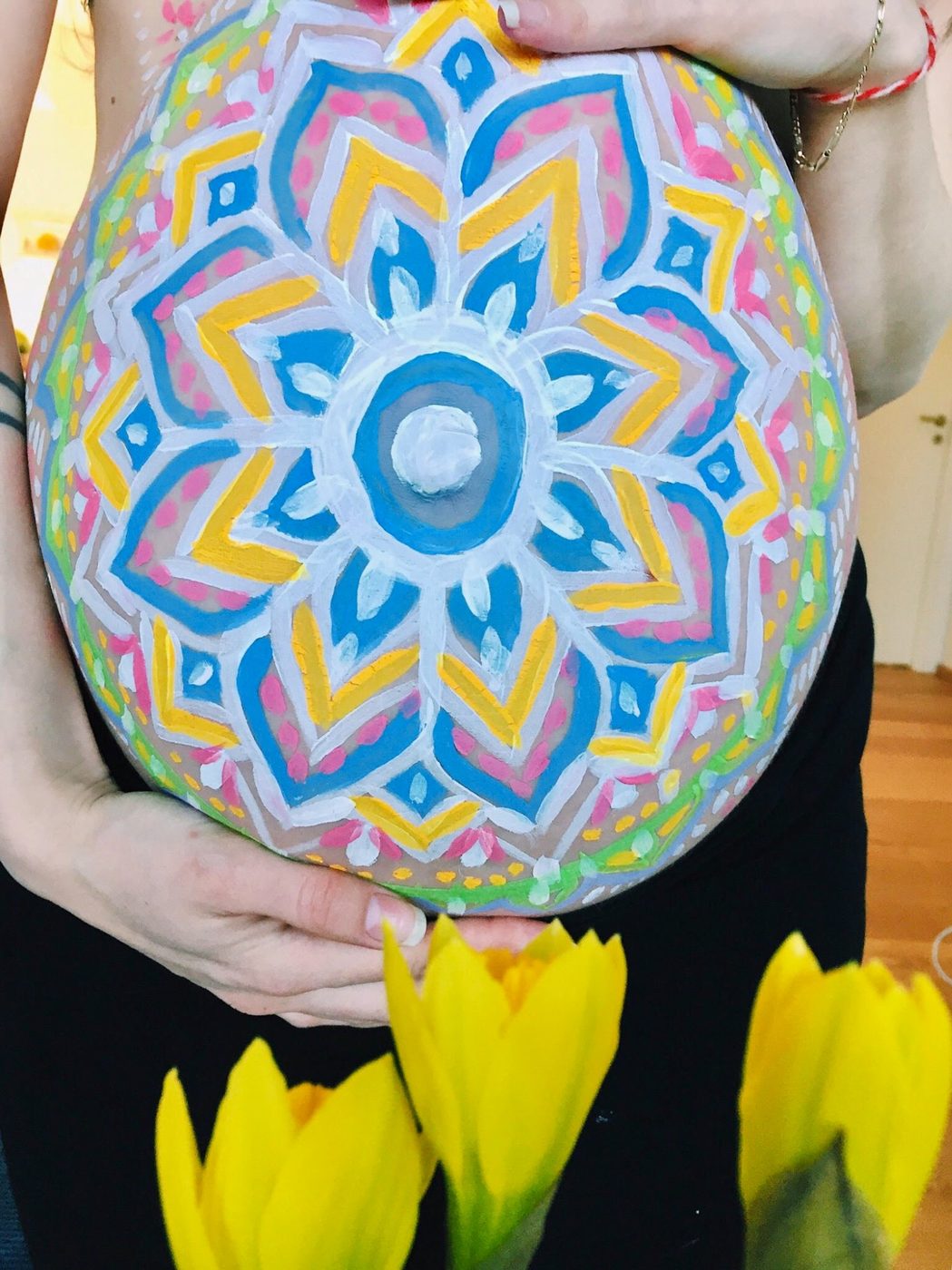 Blue and yellow mandala painted on a pregnant belly with sunflowers