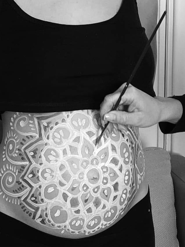 Lasma painting a white mandala on a pregnant belly with a brush
