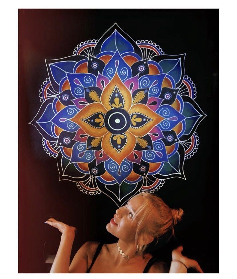 Lasma looking up at a blue, purple and orange mandala on a dark wall